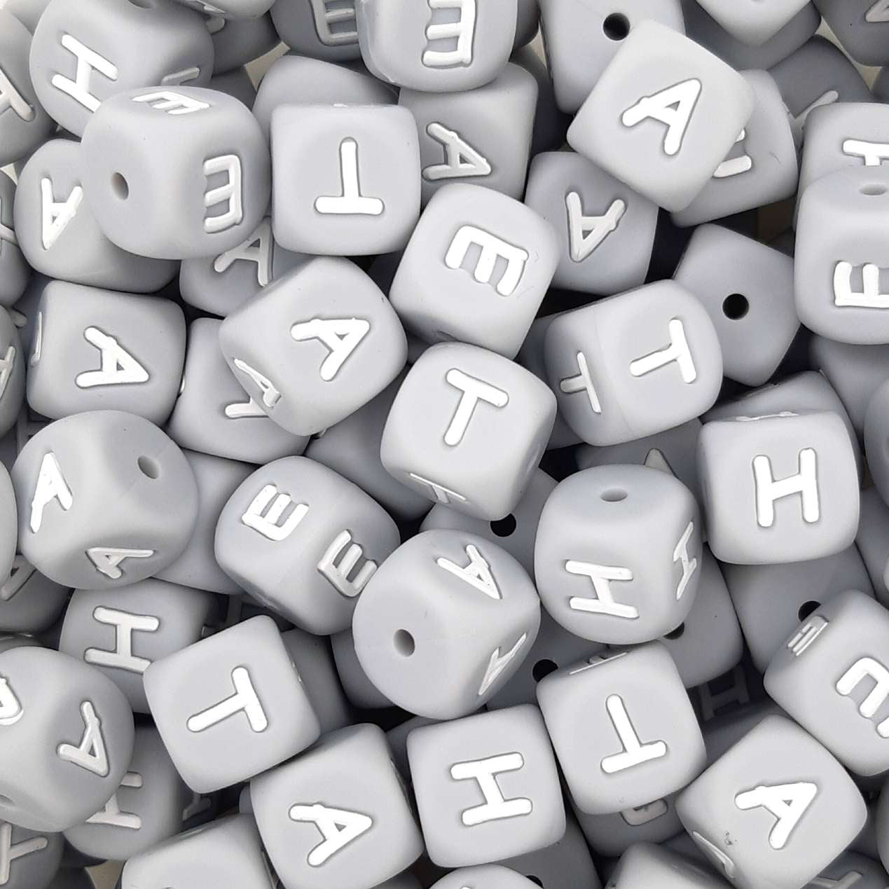 Gray letter beads with white letters scattered on a flat surface