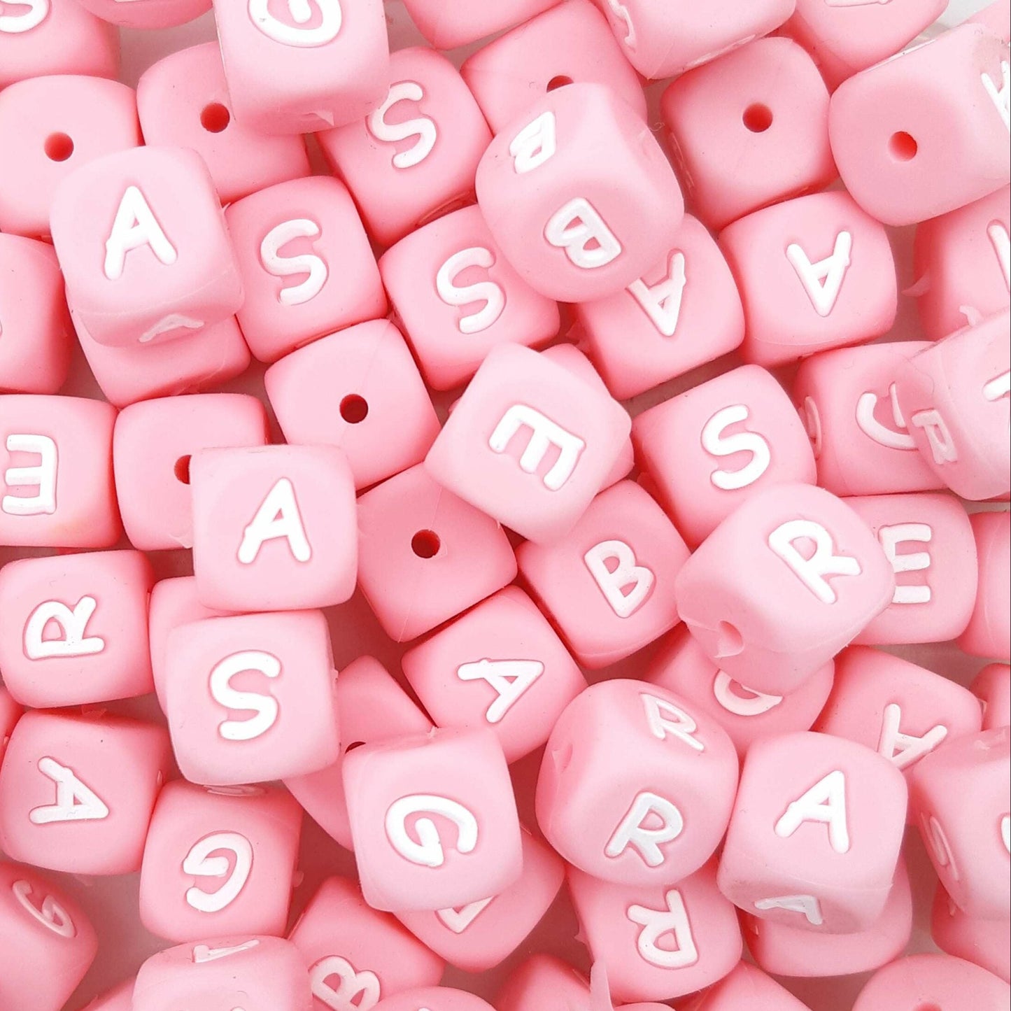 Pink letter beads with white letters scattered on a pink background