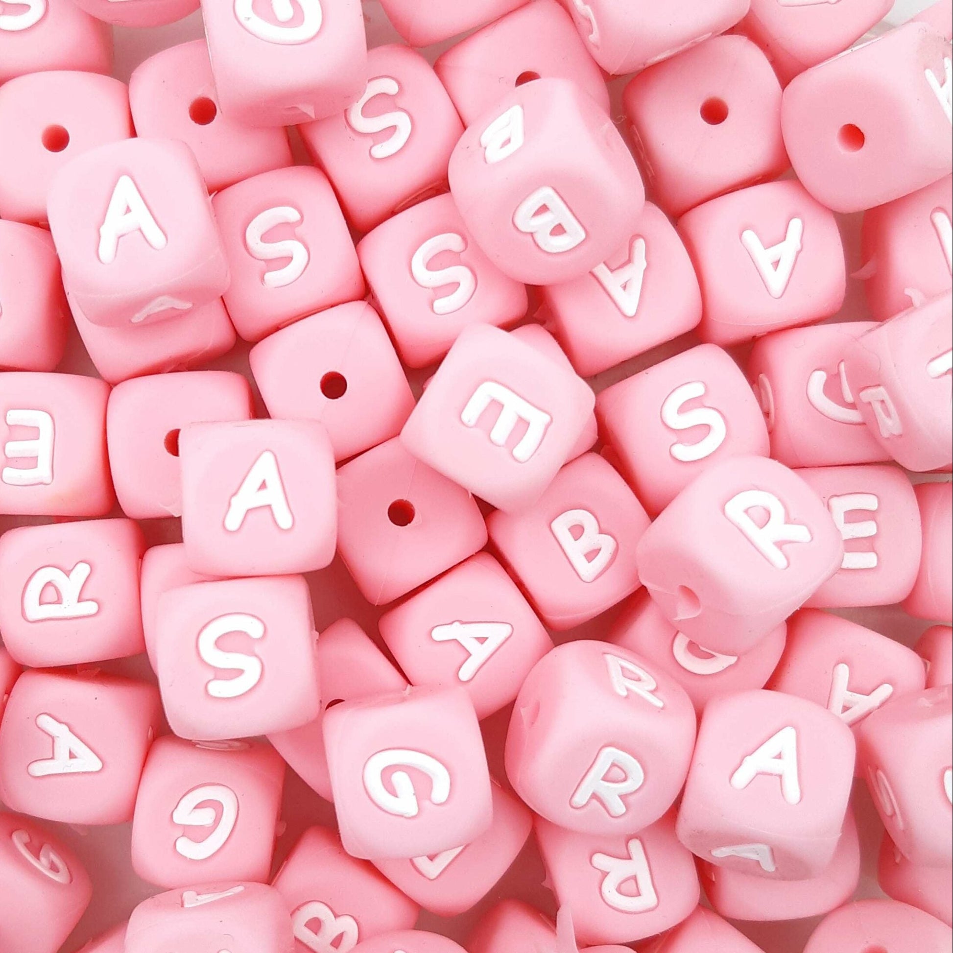 Pink letter beads with white letters scattered on a pink background